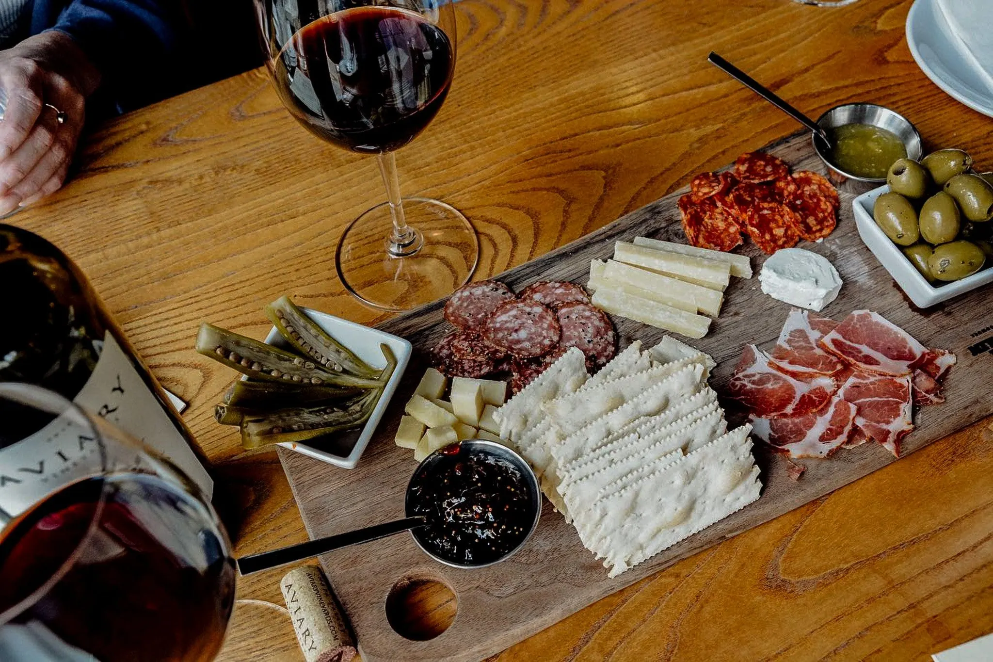 A board of cured meats, cheese, crackers and olives beside a glass of red wine